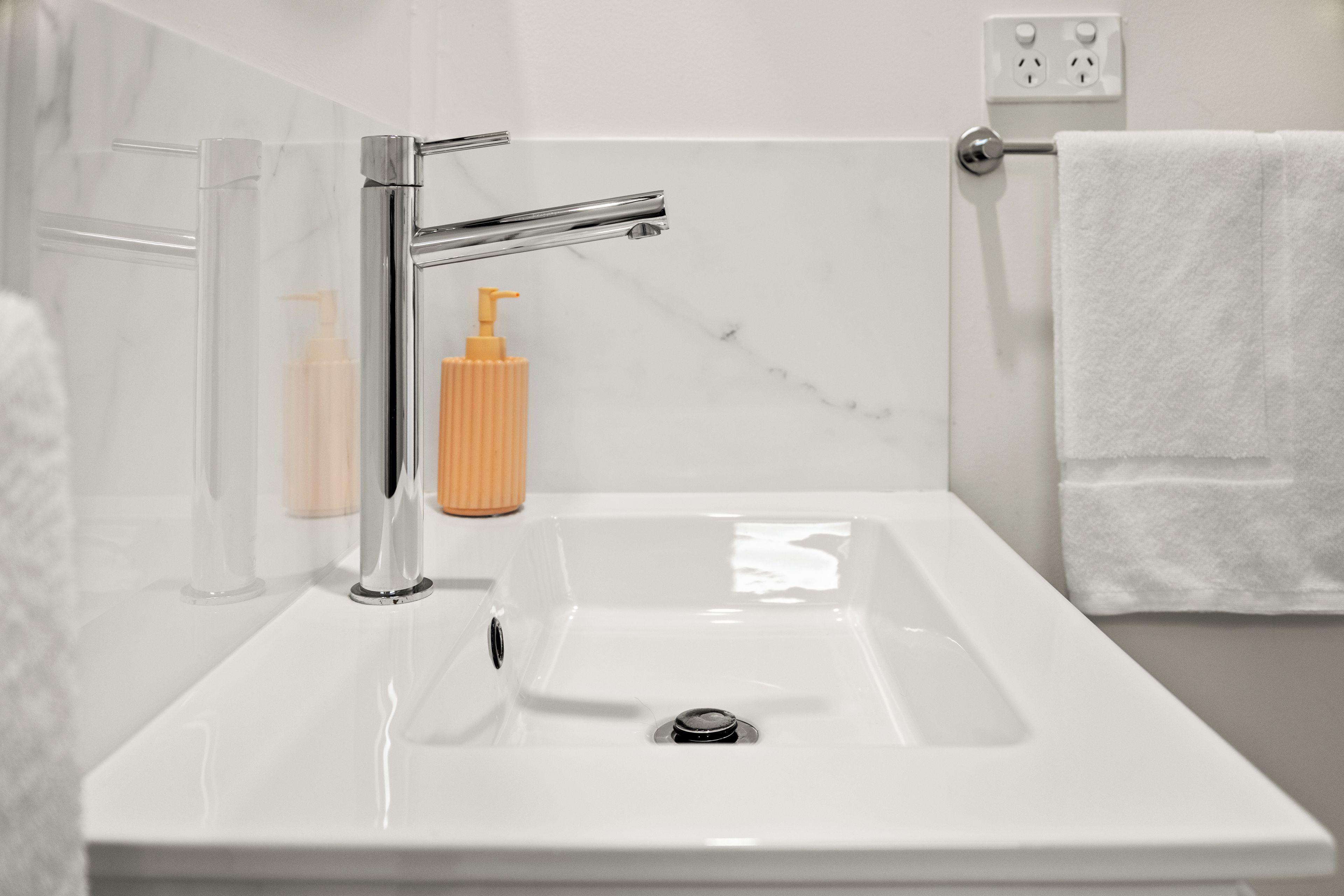 A bathroom with a white sink, chrome faucet, and a towel rack.