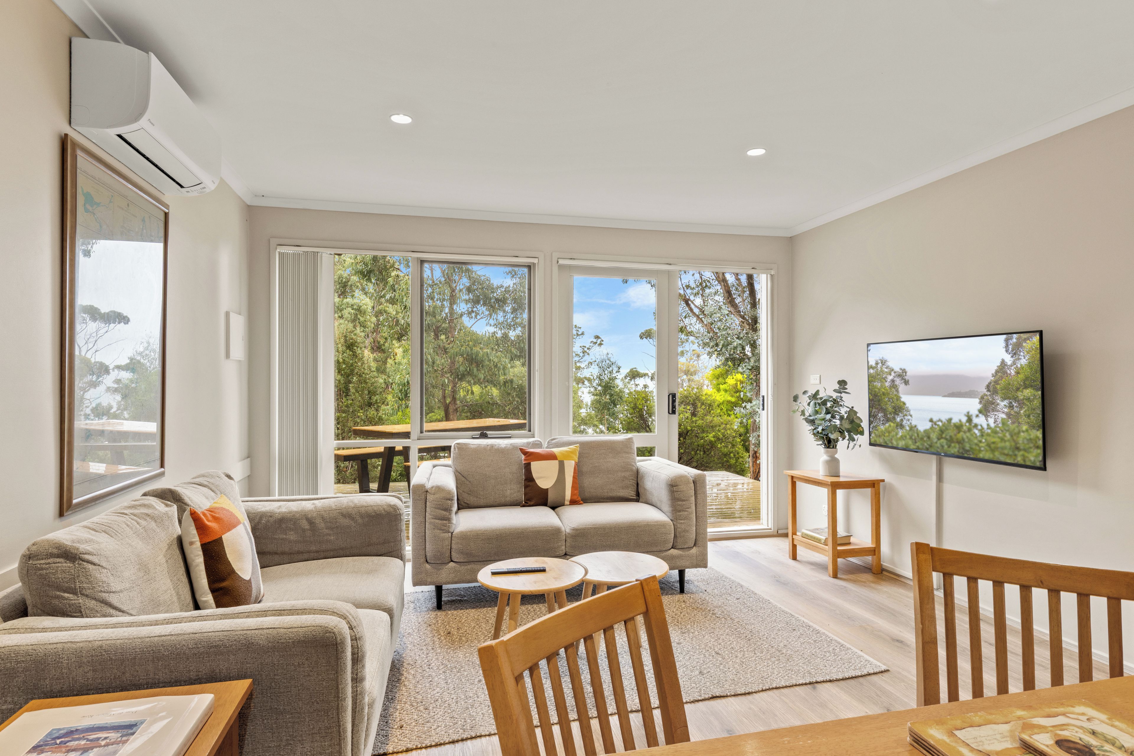 A modern living room with a sofa, armchairs, a coffee table, and a TV mounted on the wall.