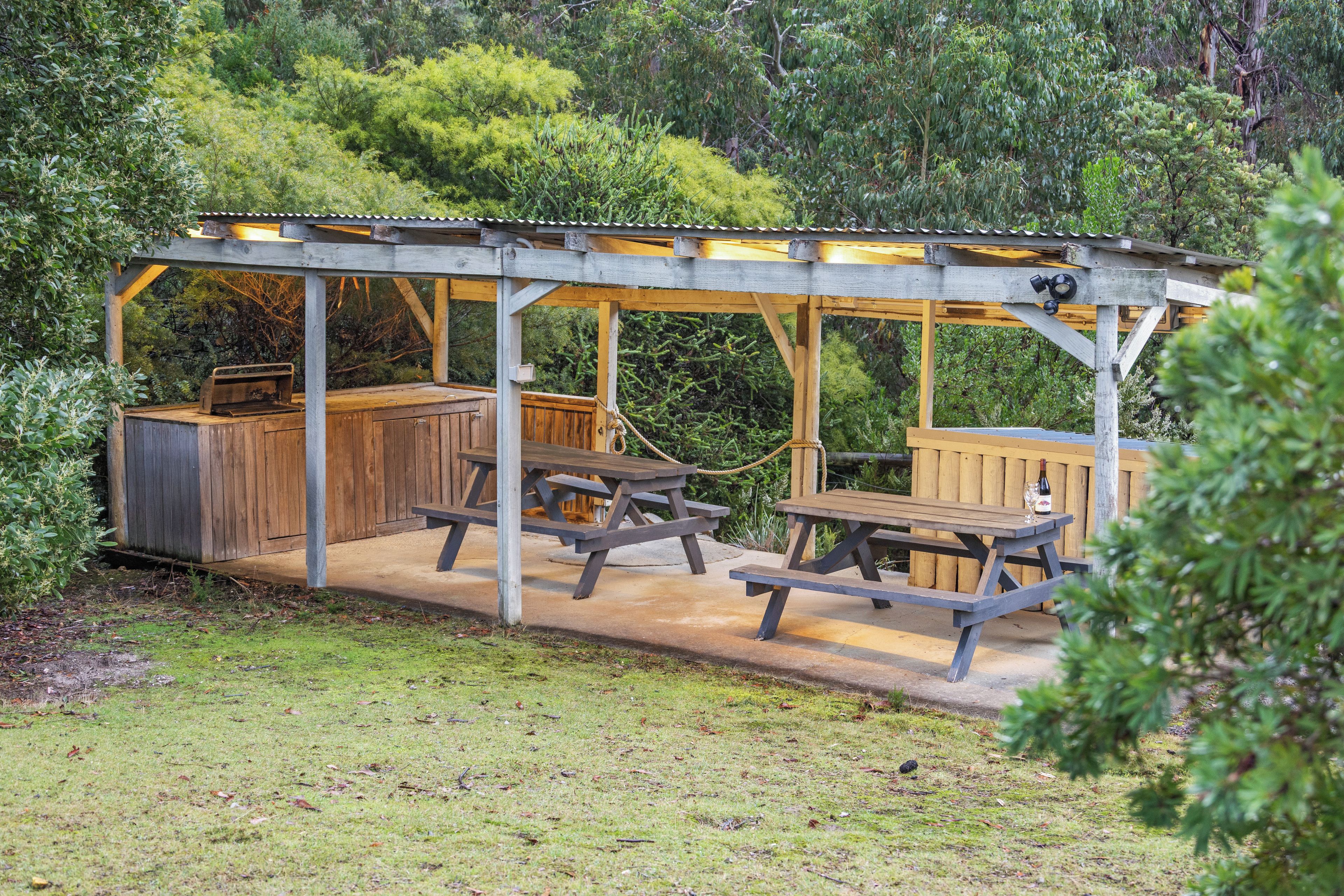 Un espacio al aire libre techado con mesas de picnic y una parrilla.