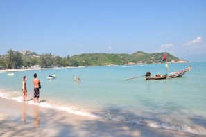 A beach with clear turquoise water, a boat, and people in the distance. - Samui Honey Cottages Beach Resort (Koh Samui)