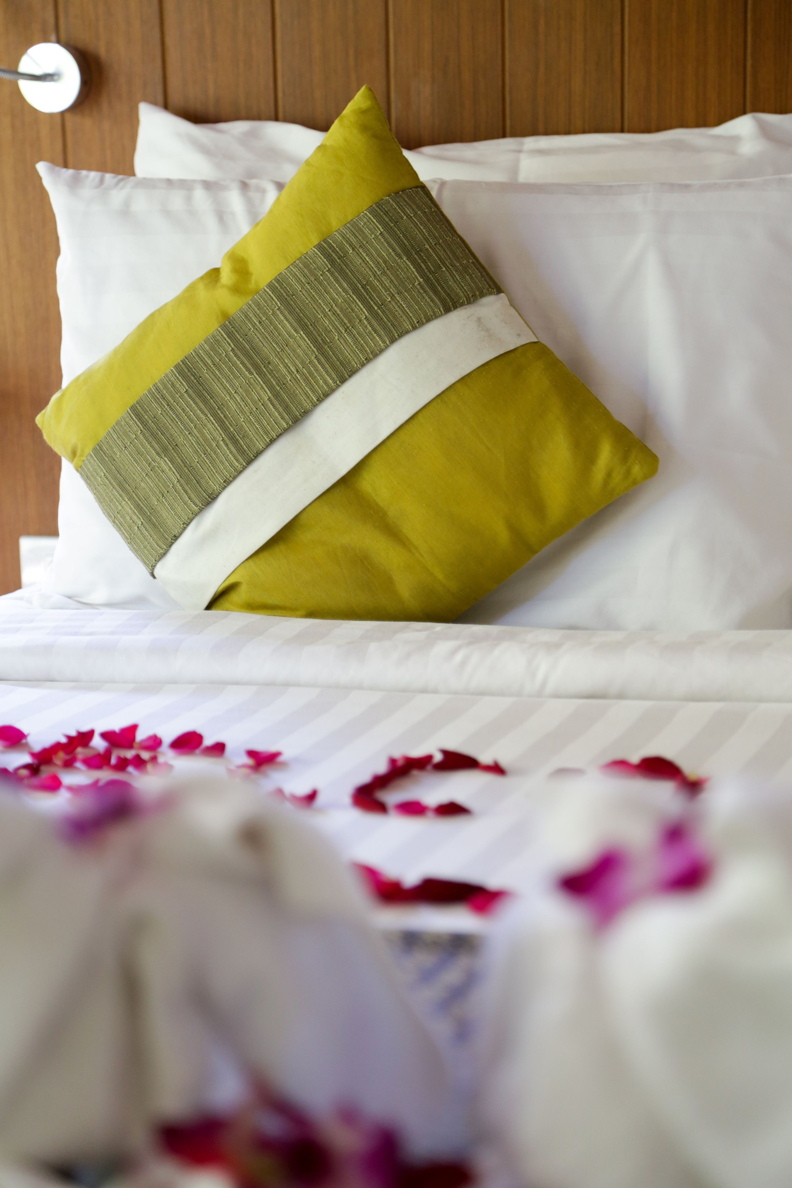Cama bien hecha con sábanas blancas y una única almohada verde y blanca.