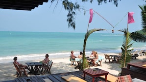 A beachside restaurant with outdoor seating, tables, and chairs, overlooking the ocean. - Samui Honey Cottages Beach Resort (Koh Samui)