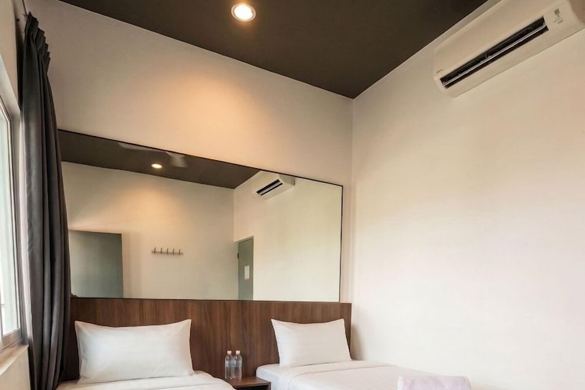 A hotel room with two single beds, a wooden headboard, a large mirror, and an air conditioning unit.