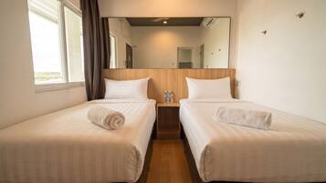 A hotel room with two single beds, a wooden headboard, a large mirror, and a window with curtains.