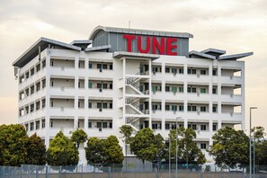 A multi-story building with a prominent 'TUNE' sign on the top. It features balconies on each floor and a central staircase.