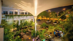 An outdoor dining area with tables and chairs under a canopy, surrounded by potted plants and a building with a glass facade. - Tune Hotel KLIA Aeropolis (Sepang)
