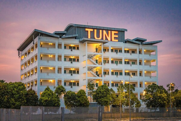A multi-story hotel with a prominent 'TUNE' sign on the top, multiple balconies, and a central staircase.
