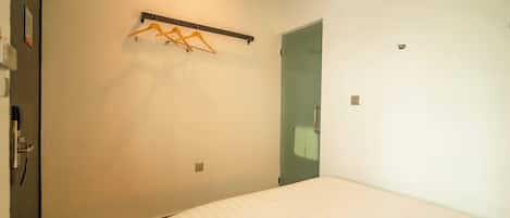 A bedroom with a bed, a wall-mounted clothes rack, a door, and an air conditioning unit.