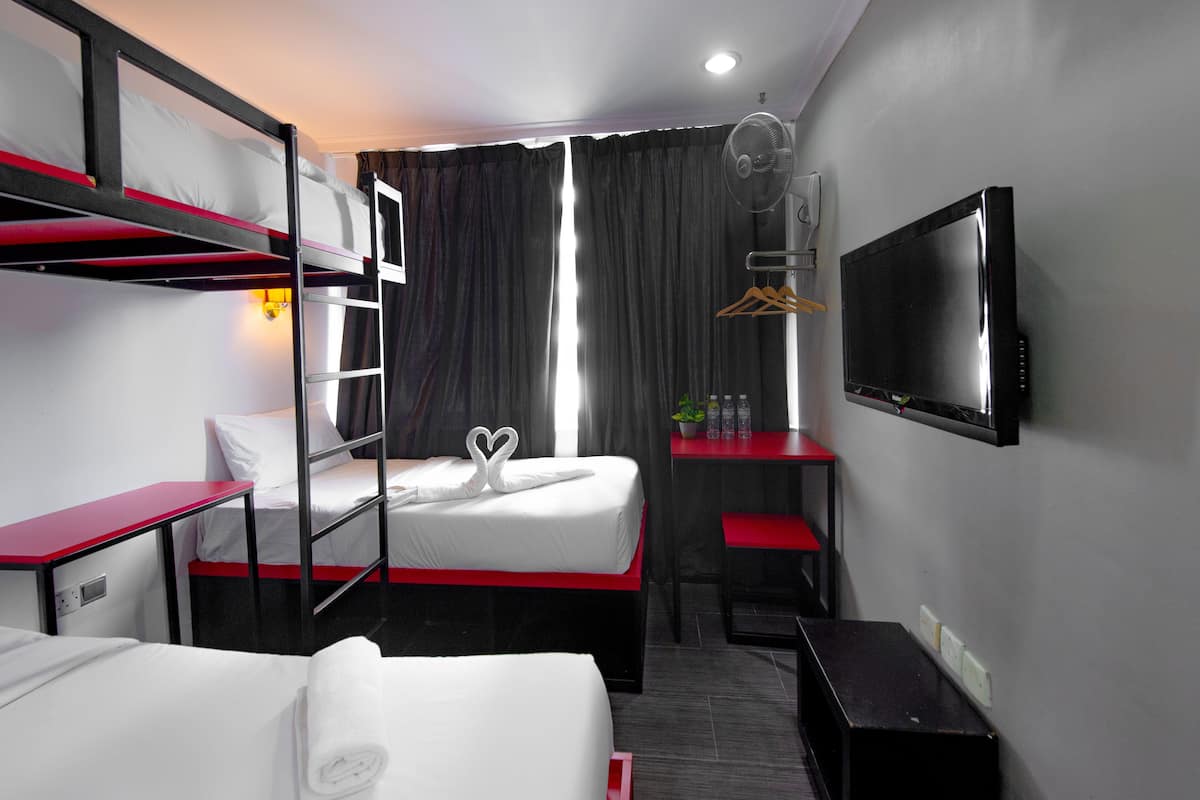 A hotel room with bunk beds, a desk, a chair, a TV, and a window with curtains.