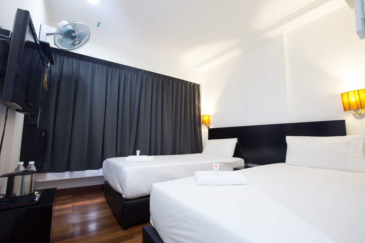 A hotel room with two beds, a TV, a fan, and a desk with a lamp.