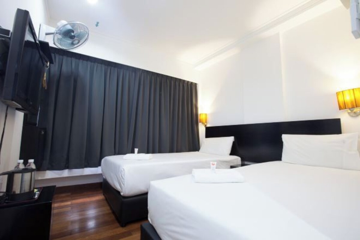 Una habitación de hotel con dos camas individuales, un televisor, un ventilador y un escritorio con lámpara.