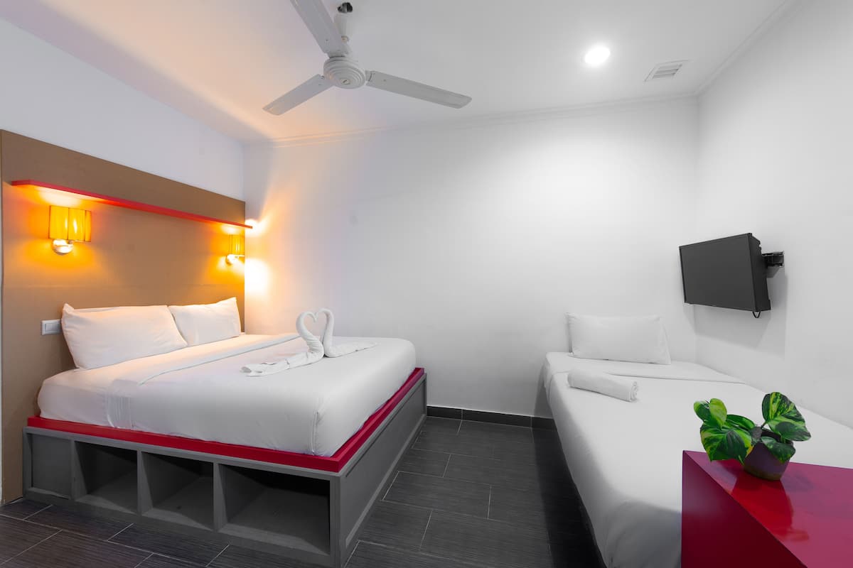 Ein Hotelzimmer mit einem Bett, einem Einzelbett, einem Deckenventilator, einem an der Wand montierten Fernseher und einer Pflanze auf einem Tisch.
