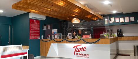 A reception desk with a wooden ceiling, a bench, and a sign for Tune Hotels.com.