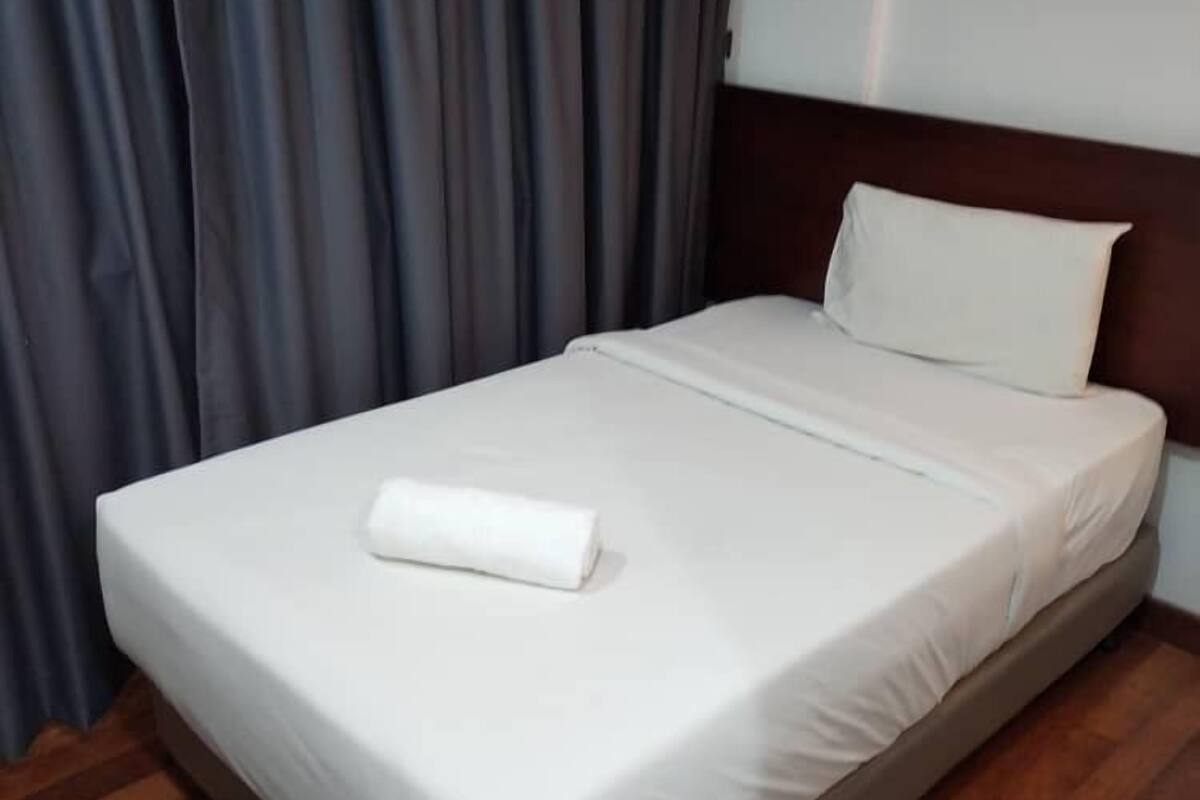 A neatly made bed with a white duvet and pillow, a wooden headboard, and a wooden floor.