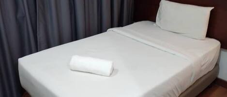 Un lit bien fait, avec une couette et un oreiller blancs, une tête de lit en bois et un plancher en bois.