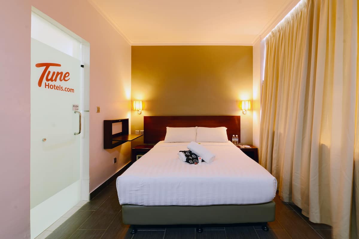 A hotel room with a bed, a nightstand, a lamp, and a door with a sign.
