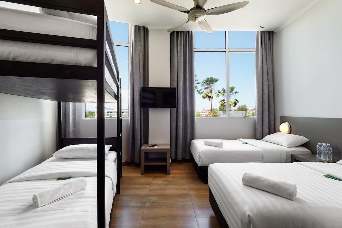 A hotel room with bunk beds, a flat-screen TV, a bedside table, and a window with a view of palm trees.
