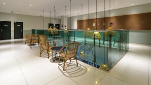 A modern hotel lobby with a glass partition, wicker chairs, and pendant lighting. - Tune Hotels - 1 Borneo, Kota Kinabalu (Kota Kinabalu)