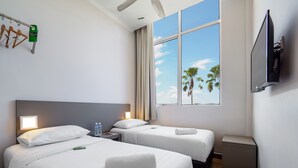 A hotel room with two beds, a TV, a window with a view of palm trees, and a ceiling fan. - Tune Hotels - 1 Borneo, Kota Kinabalu (Kota Kinabalu)