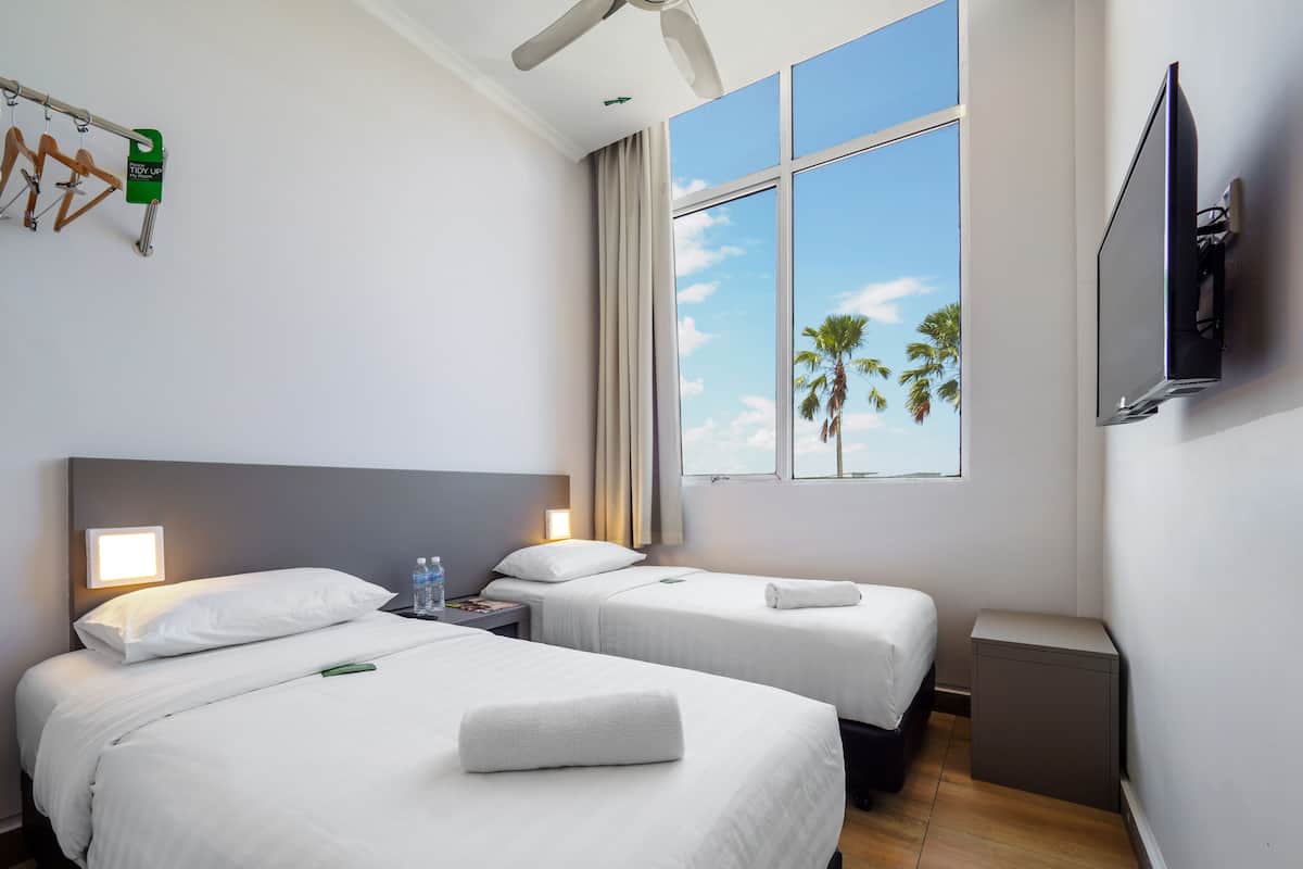 A hotel room with two beds, a TV, a window with a view of palm trees, and a ceiling fan.