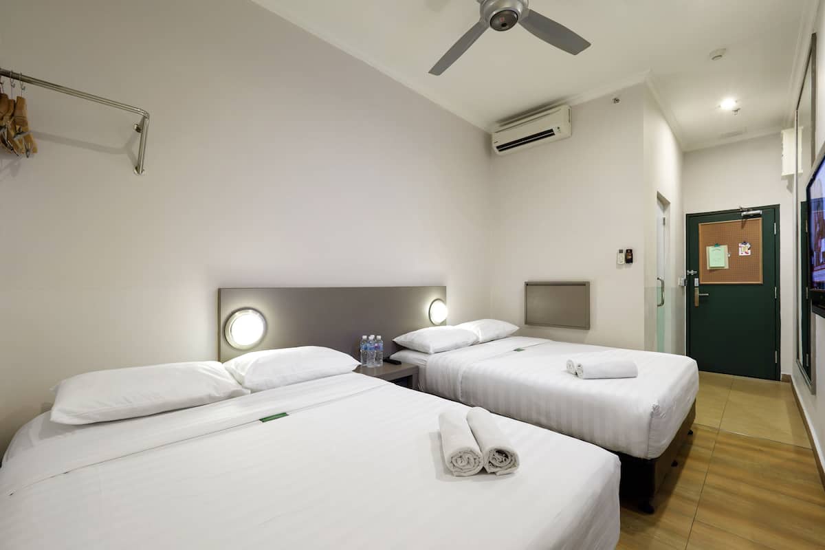A hotel room with two beds, a ceiling fan, an air conditioning unit, a TV, and a door with a bulletin board.