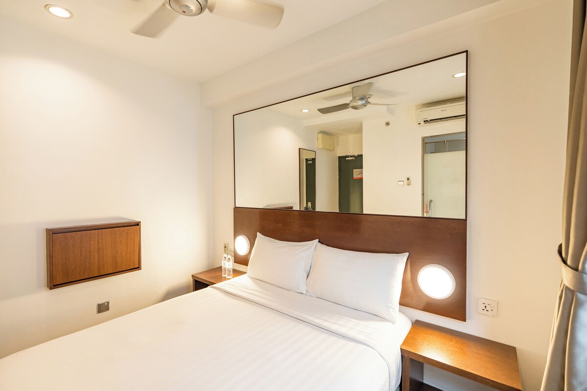 A hotel room with a large bed, a wooden headboard, a mirror, bedside lamps, and a ceiling fan.