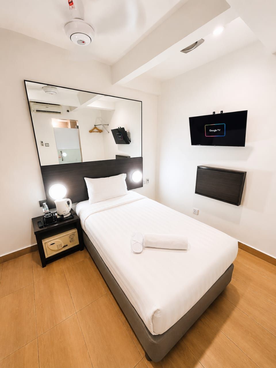 Une chambre d’hôtel comprenant un lit, une table de chevet avec une lampe, un téléviseur à écran plat, un grand miroir et un téléviseur fixé au mur.
