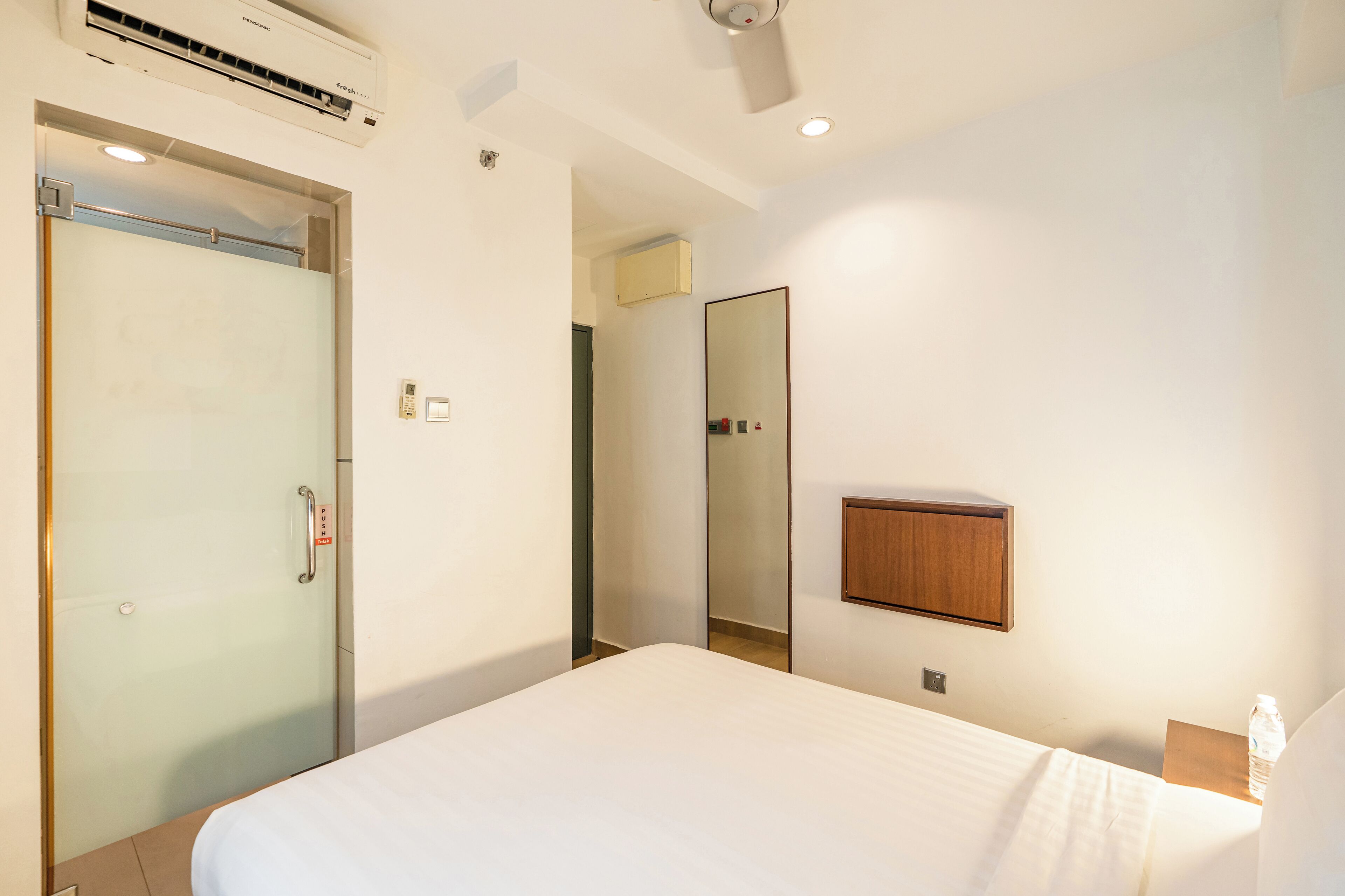 Una habitación de hotel con cama, puerta, espejo y un mueble pequeño.