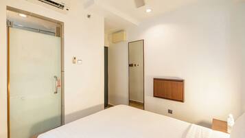 Una habitación de hotel con cama, puerta, espejo y un mueble pequeño.