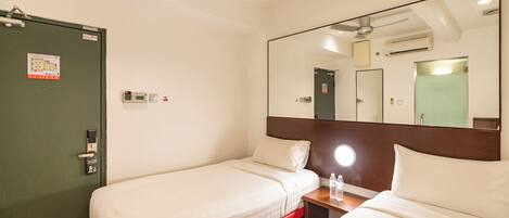 A hotel room with two single beds, a bedside table with a lamp, a large mirror, and a ceiling fan.