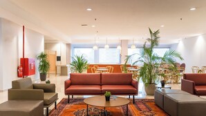 A modern lobby with a red sofa, grey armchairs, a coffee table, and a patterned rug. - NIO Hotel (George Town)