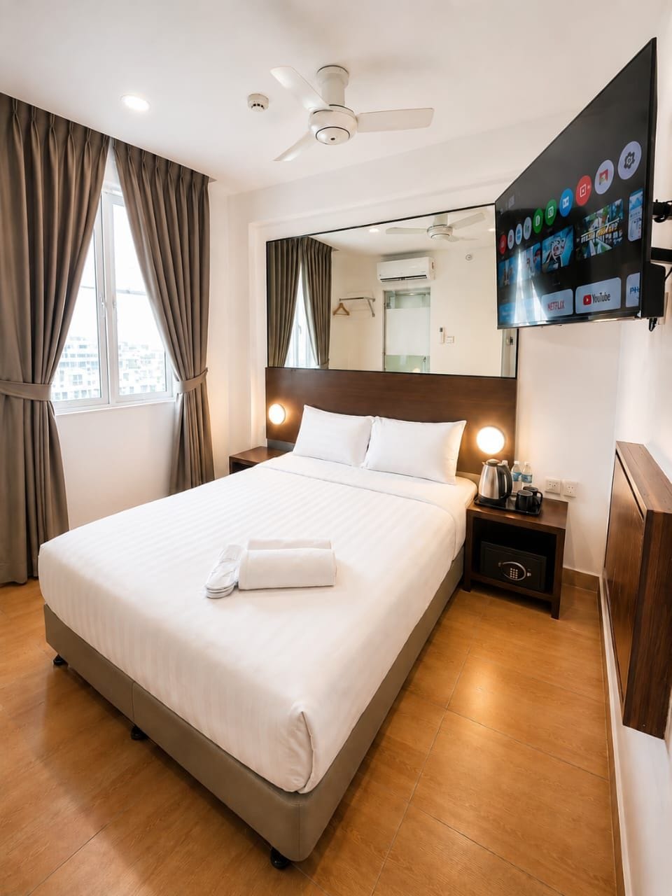 Une chambre d’hôtel avec un lit, une table de chevet, une télévision et une fenêtre avec des rideaux.
