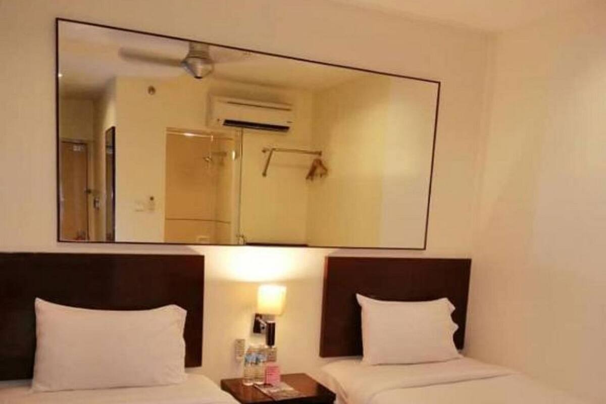 Ein Hotelzimmer mit zwei Betten, einem großen Spiegel, einem Nachttisch mit Lampe und einer Klimaanlage.