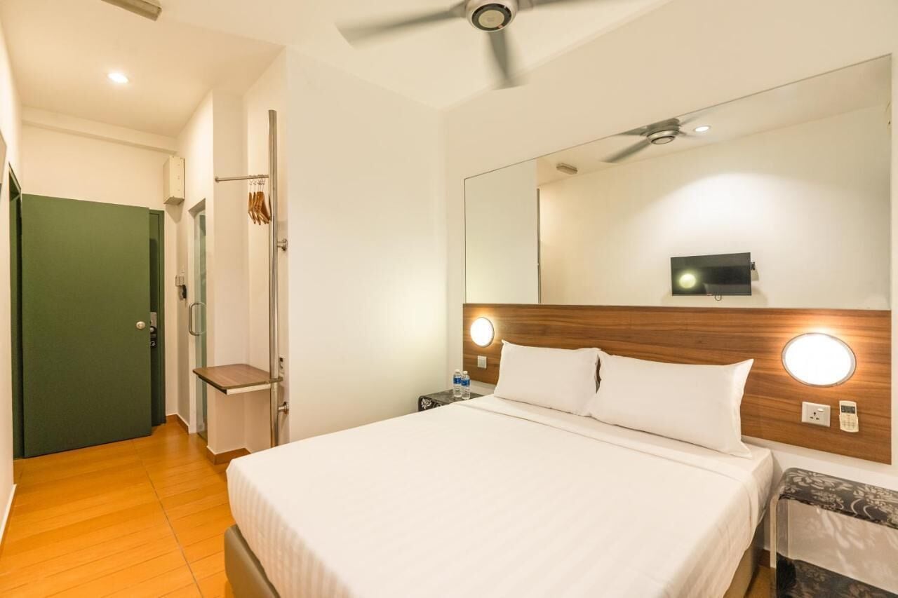 Habitación de hotel con cama, mesita de noche, espejo, ventilador de techo y una puerta verde.