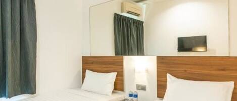 Una habitación de hotel con dos camas, un ventilador de techo, un equipo de aire acondicionado, una mesita de noche con lámpara y un espejo grande en la pared.