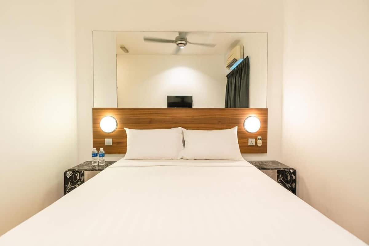 Une chambre d’hôtel avec un grand lit, une tête de lit en bois, deux tables de chevet avec des lampes, un ventilateur de plafond et un téléviseur à écran plat.