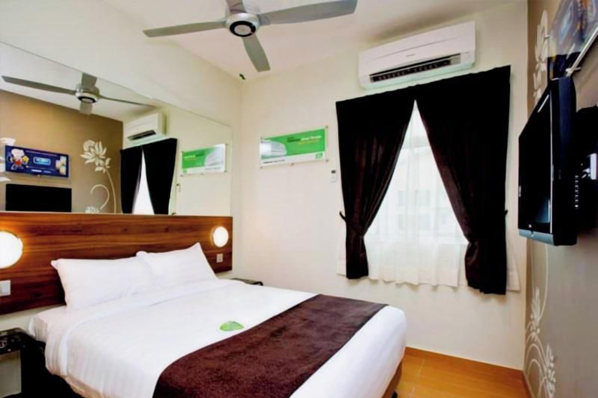 Een hotelkamer met een bed, een plafondventilator, een airconditioning, een televisie en een raam met gordijnen.