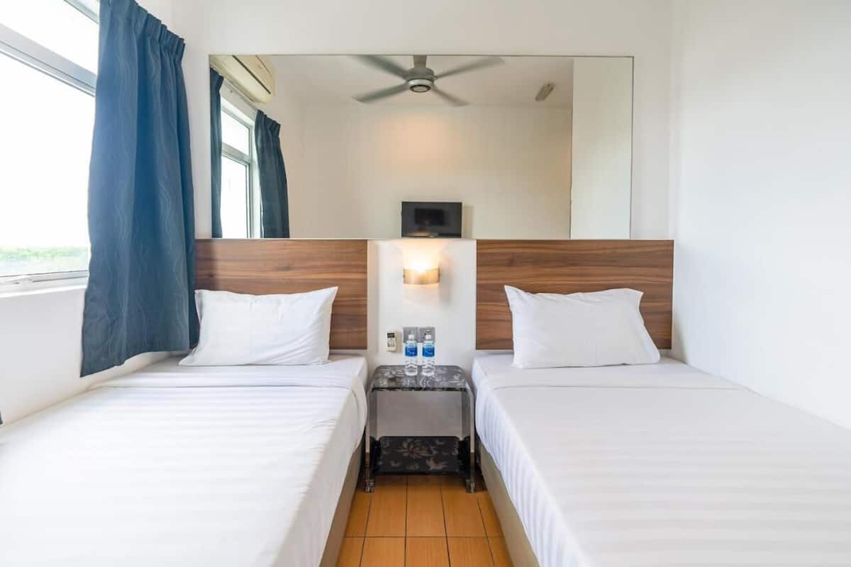 Une chambre d’hôtel avec deux lits, un ventilateur de plafond, une table de chevet avec une lampe et une fenêtre avec des rideaux.
