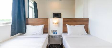 A hotel room with two beds, a ceiling fan, a nightstand with a lamp, and a window with curtains.