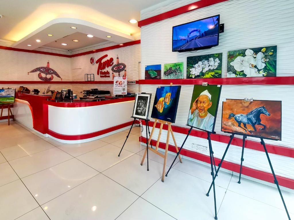A reception area with a red and white color scheme, a TV mounted on the wall, and several paintings displayed on easels.