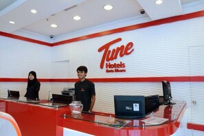 Ein Empfangsschalter mit rotem und weißem Farbschema, eine Schilder mit der Aufschrift "Tune Hotels Kota Bharu" und eine Überwachungskamera darüber.