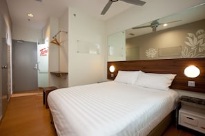 Ein Hotelzimmer mit einem großen Bett, einem Nachttisch mit Lampe, einem Spiegel, einem Deckenventilator und einem Schild für Tune Hotels.