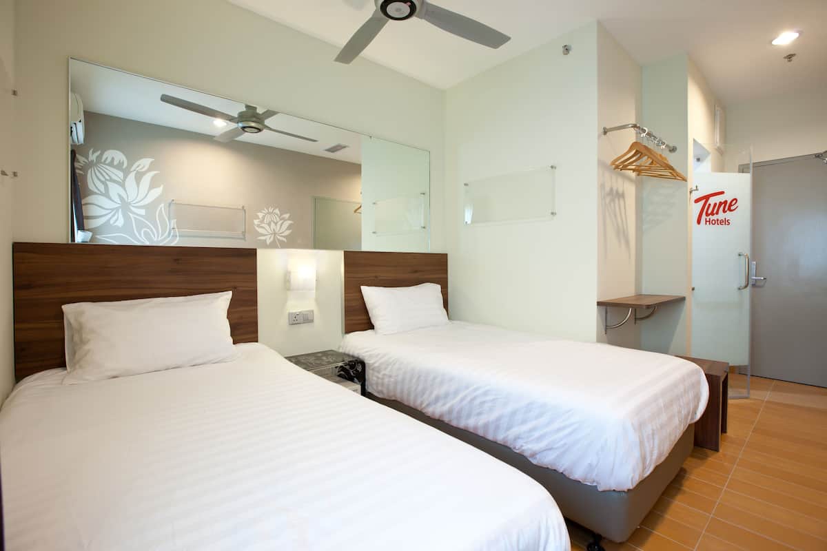 Une chambre d’hôtel avec deux lits, un ventilateur de plafond, un miroir et une armoire portant l’inscription « Tune Hotels ».