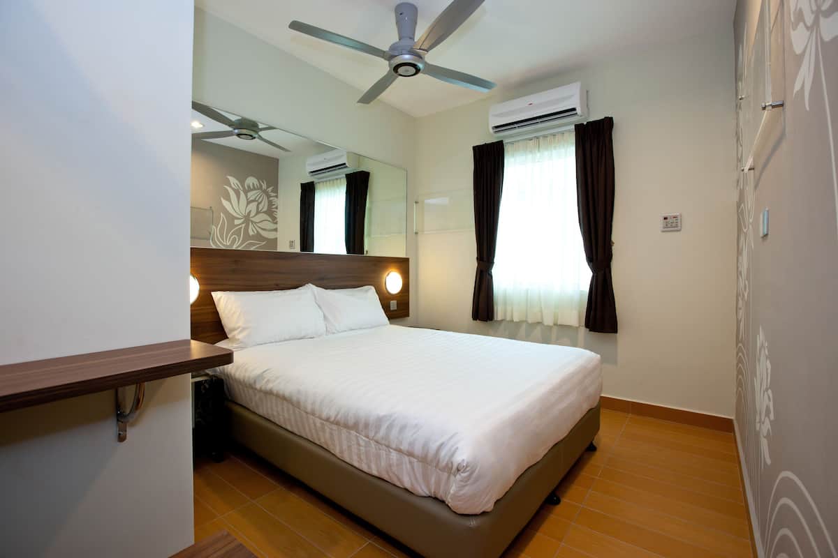 Une chambre d’hôtel équipée d’un lit, d’un ventilateur de plafond, d’un appareil de climatisation, d’un miroir et d’une fenêtre avec des rideaux.