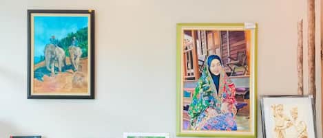 Una pared con varias obras de arte enmarcadas, incluyendo una pintura de elefantes y una figura colorida.