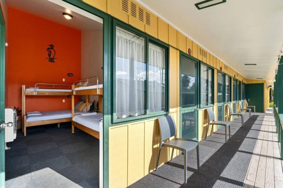 A hostel room with bunk beds, a small kitchenette, and a seating area with chairs and a table.