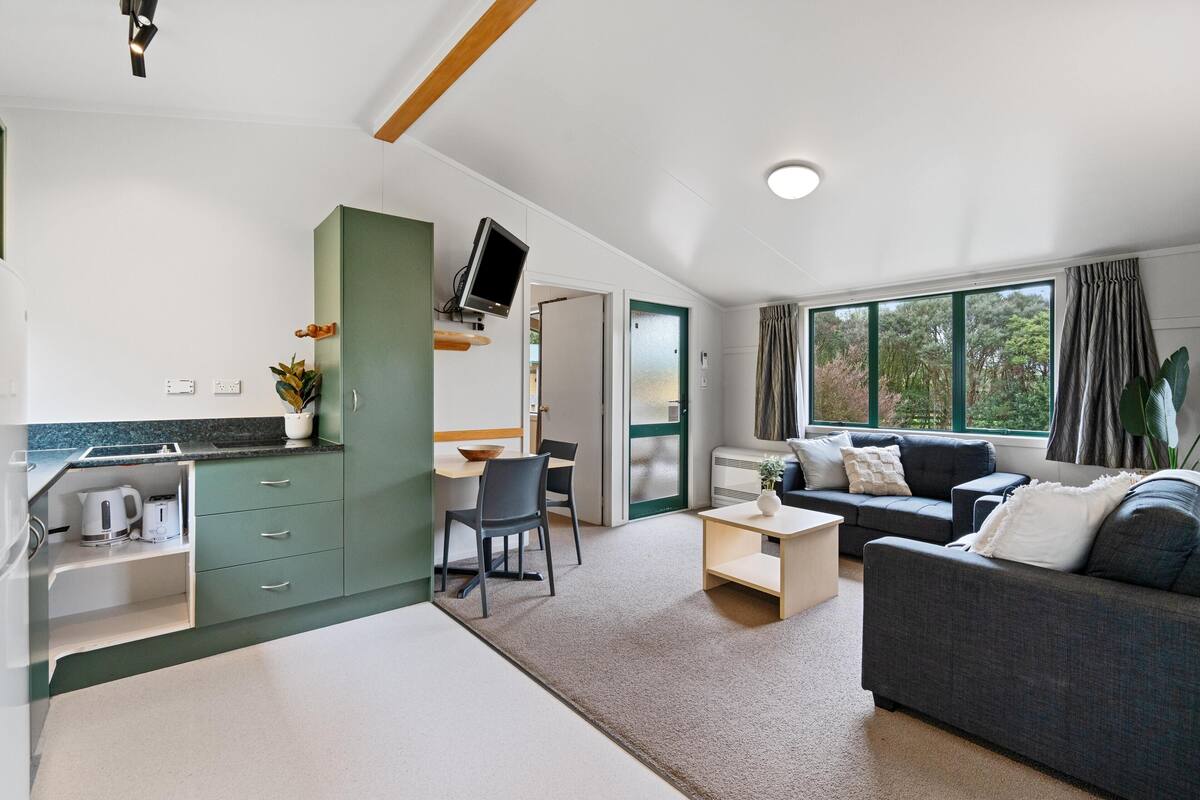 A modern living room with a grey sofa, a coffee table, and a TV mounted on a green cabinet.