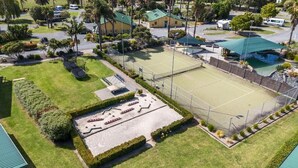 Oversigtsbillede af et resort med tennisbane, pool og flere bygninger, omgivet af palmer og grønt