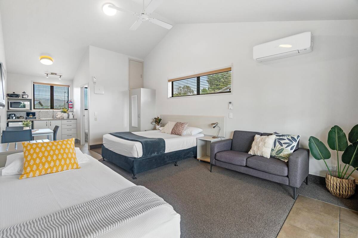 A modern hotel room with a bed, a sofa, a desk, and a small kitchenette.