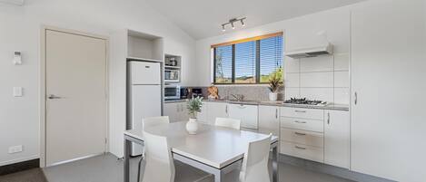 A modern kitchen with white cabinetry, a dining table with chairs, a built-in oven, and a window with a view of the outdoors.